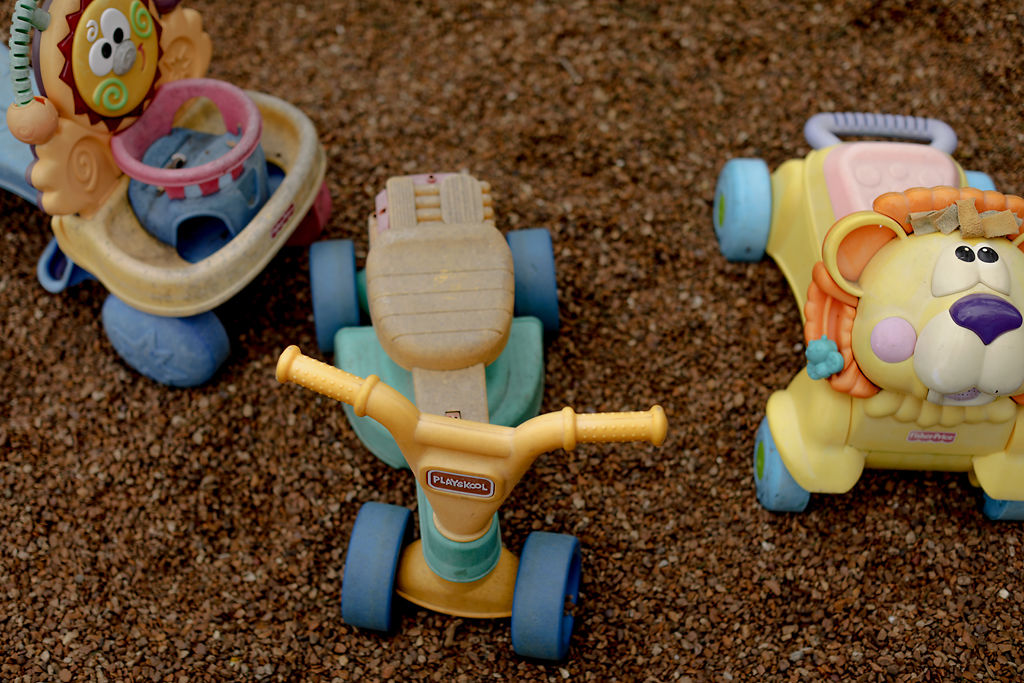 Assorted child transportation vehicles sit inside of a pebble-filled play area